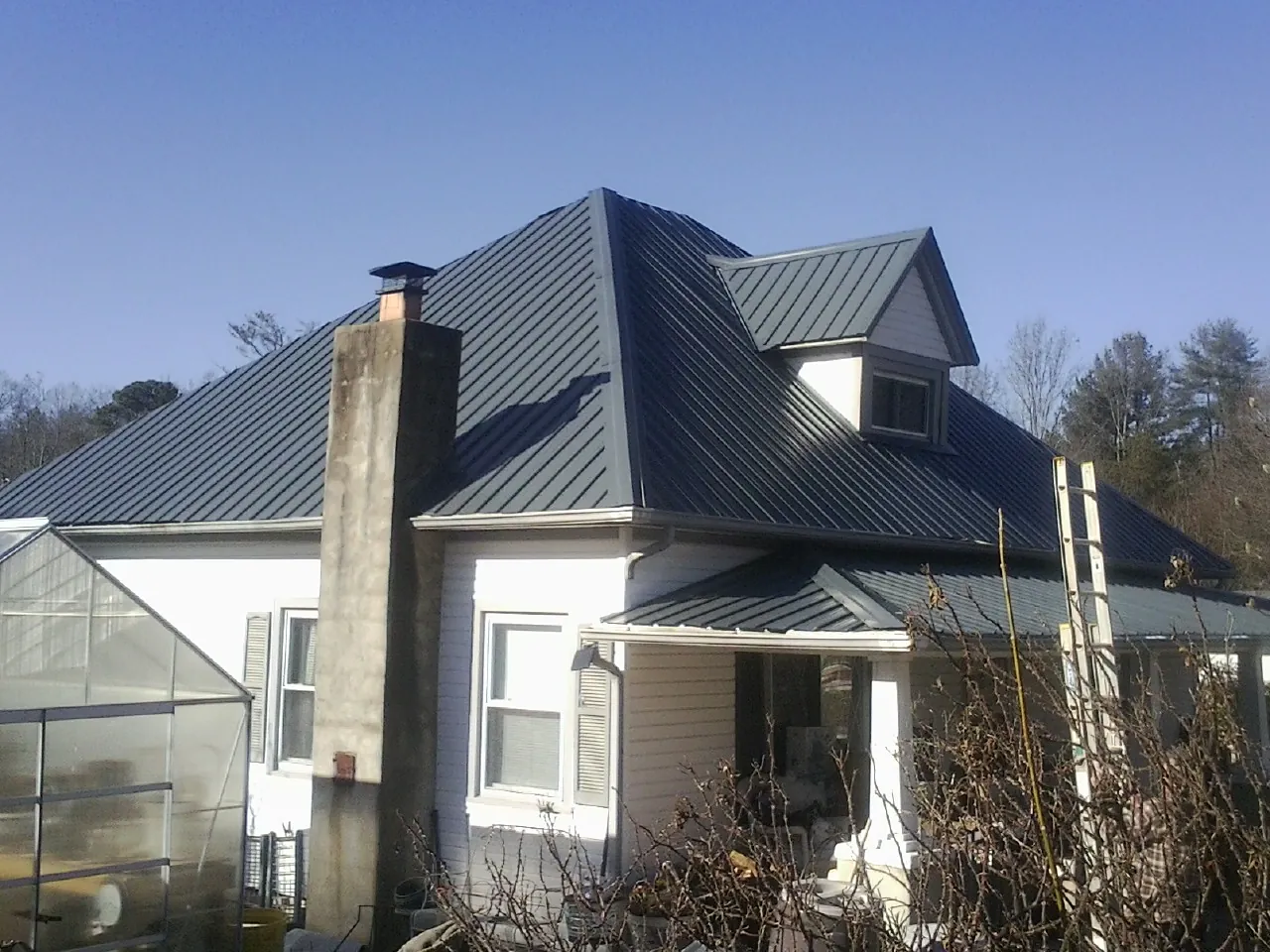 Dark blue standing seam metal roof on a white farmhouse with dormer — Slate & Tile Roof Repair by Roofing Brothers in New Century