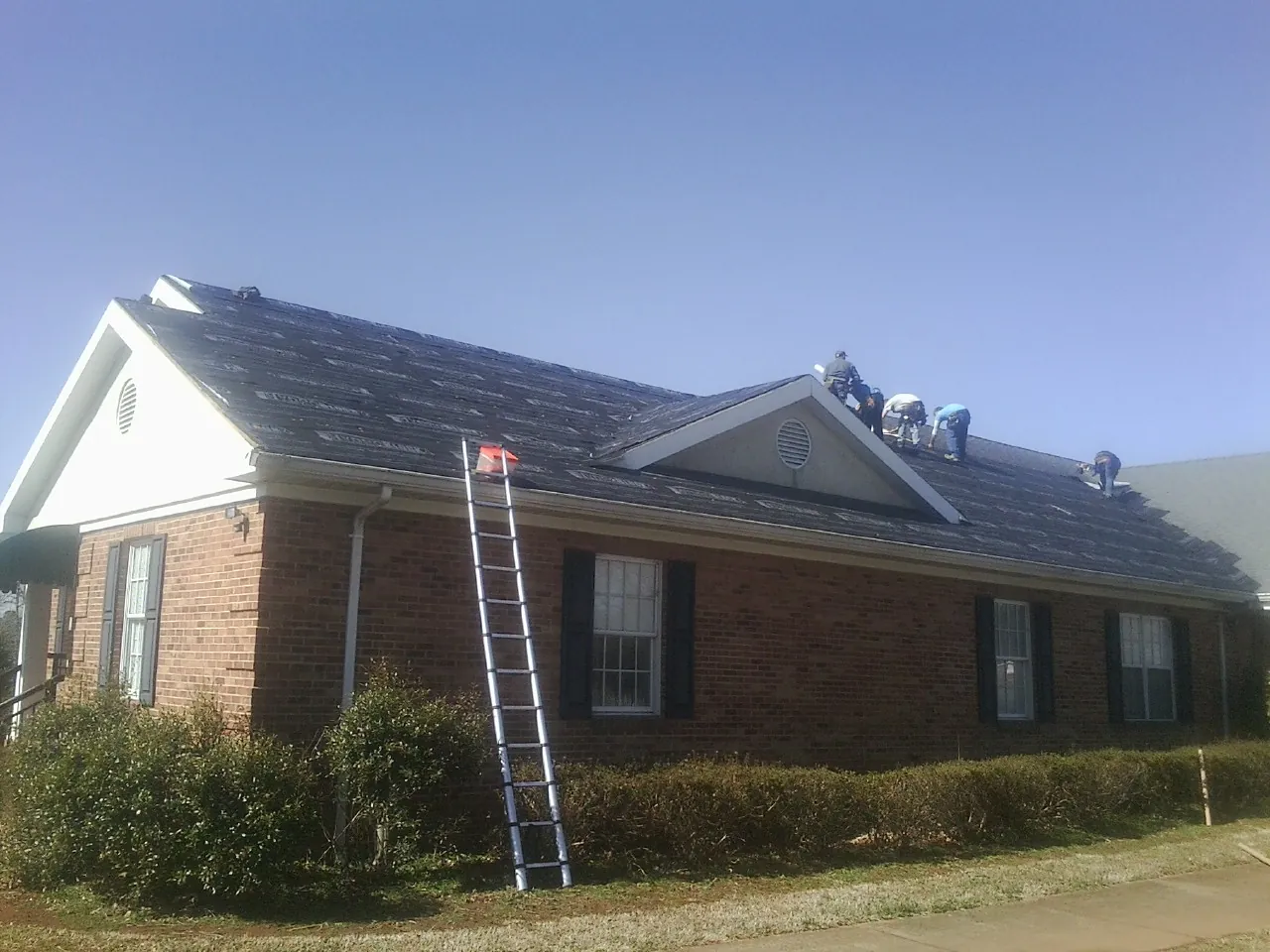Crew tearing shingles off a brick ranch roof with a ladder set — Metal Roof Repair work by our crew in New Century