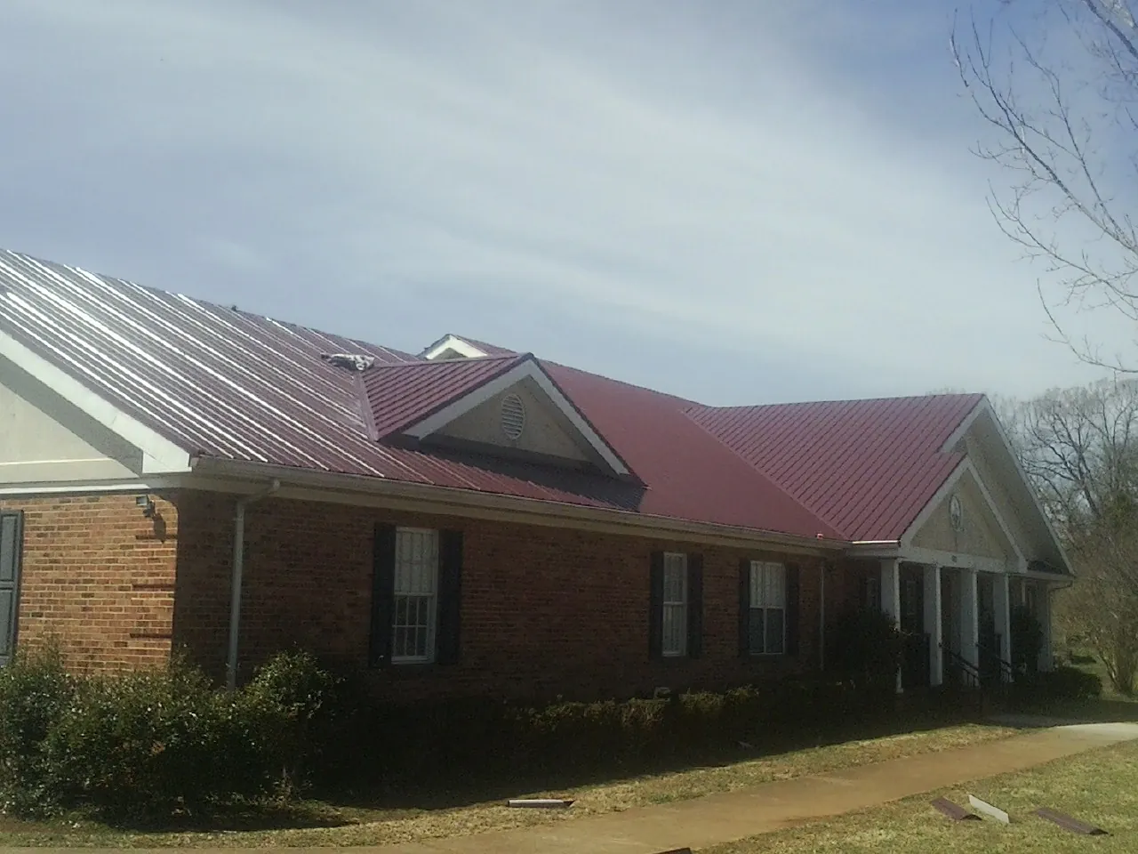 Red metal roof with gabled entries on a long brick building, from a Hail Damage Roof Repair job in New Century