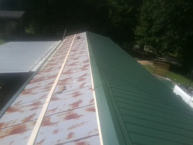 Old rusted panels beside newly installed green metal roofing — Wind Damage Roof Repair by Roofing Brothers in New Century
