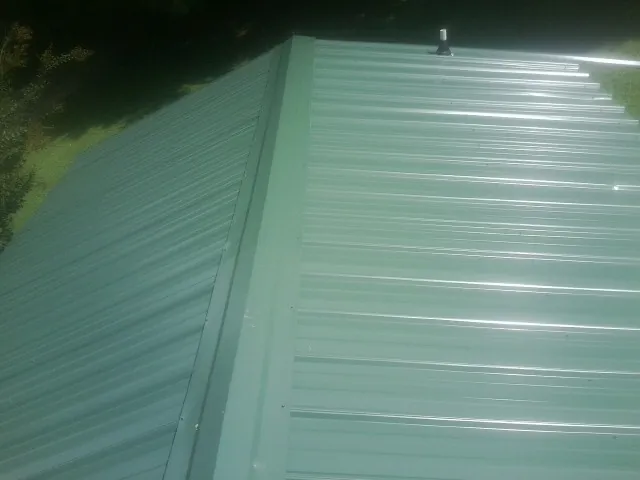 New green metal panels meeting at the ridge of a roof — Flat Roof Repair work by our crew in New Century