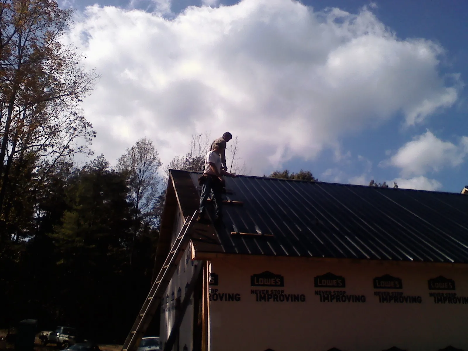 Roofer fastening dark metal panels high against a cloudy sky, from a Roof Inspection job in New Century