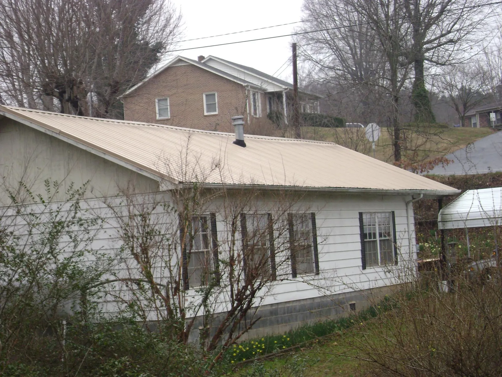 Tan metal roof on a white sided house set into a hillside — Commercial Roofing by Roofing Brothers in New Century