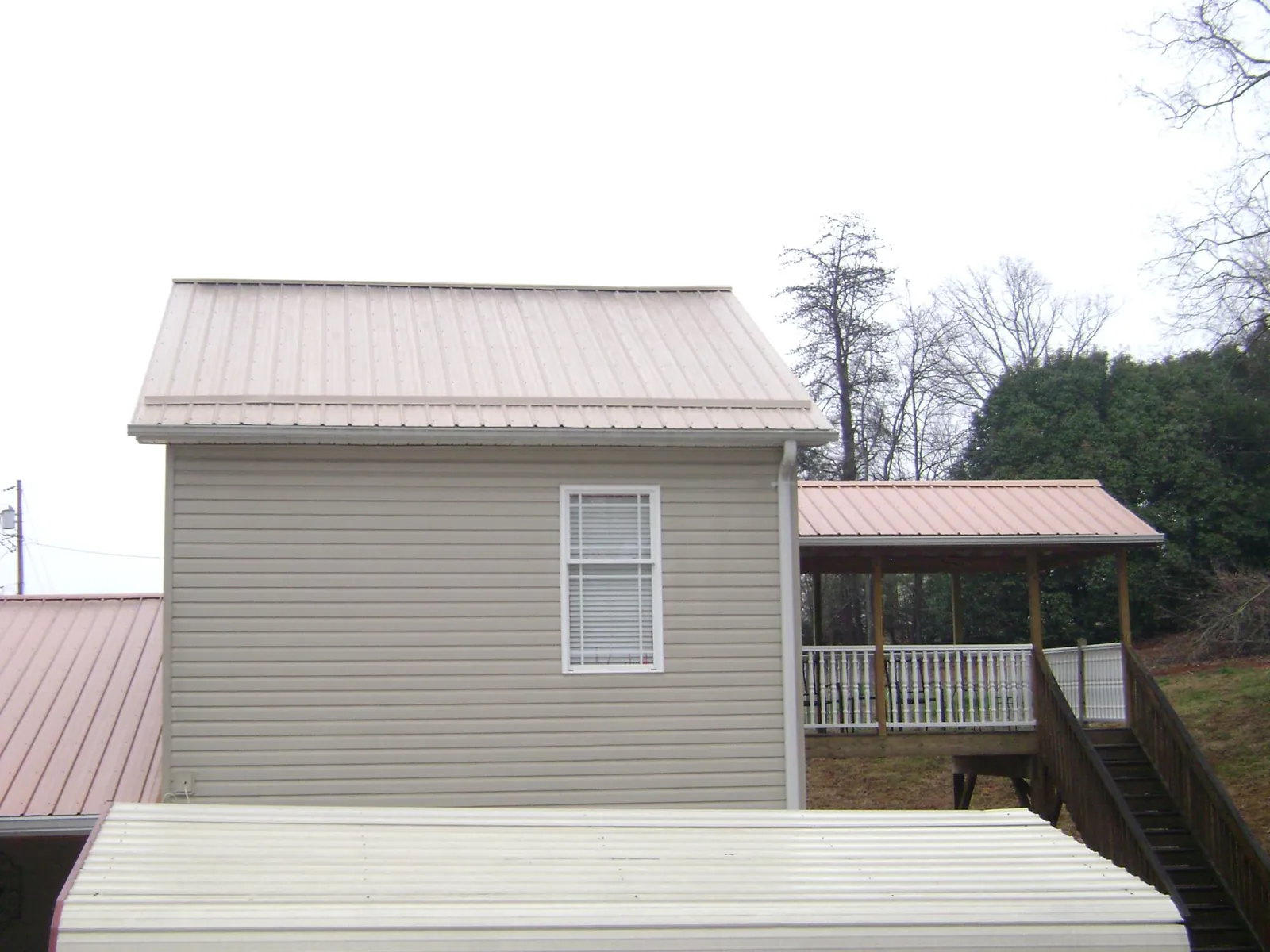 Tan metal roofs on a two story addition and attached porch, from a Roof Replacement job in New Century